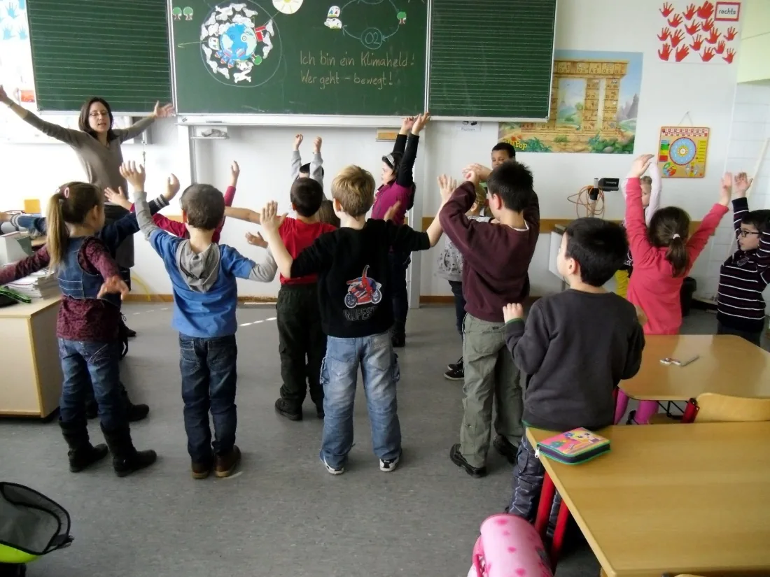 Eine ganze Klasse steht auf und macht beim Erdenrap mit, die Arme in der Luft