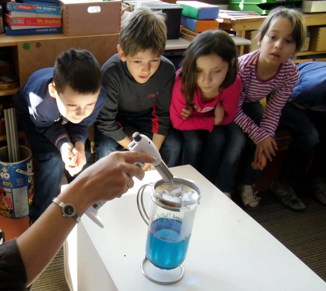 Kinder beobachten das Standglas mit Eiswürfeln, blauem Wasser und aufgeklebter Stadtsilhouette
