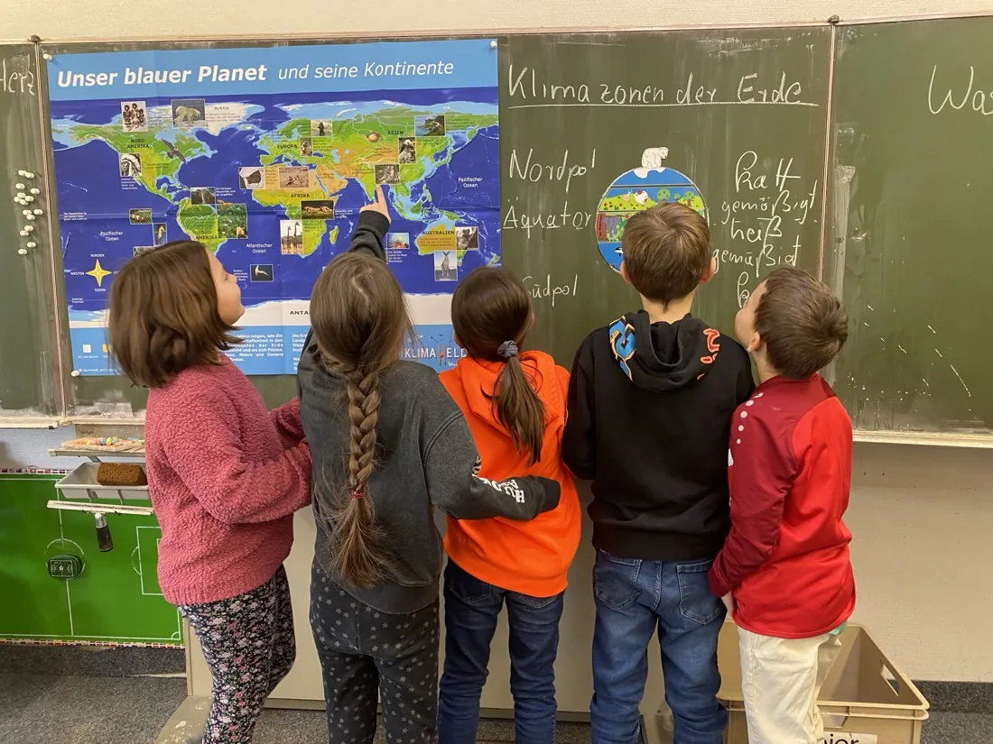Kinder zeigen an der Tafel auf die Weltkarte „Unser blauer Planet“ und die Klimazonen der Erde