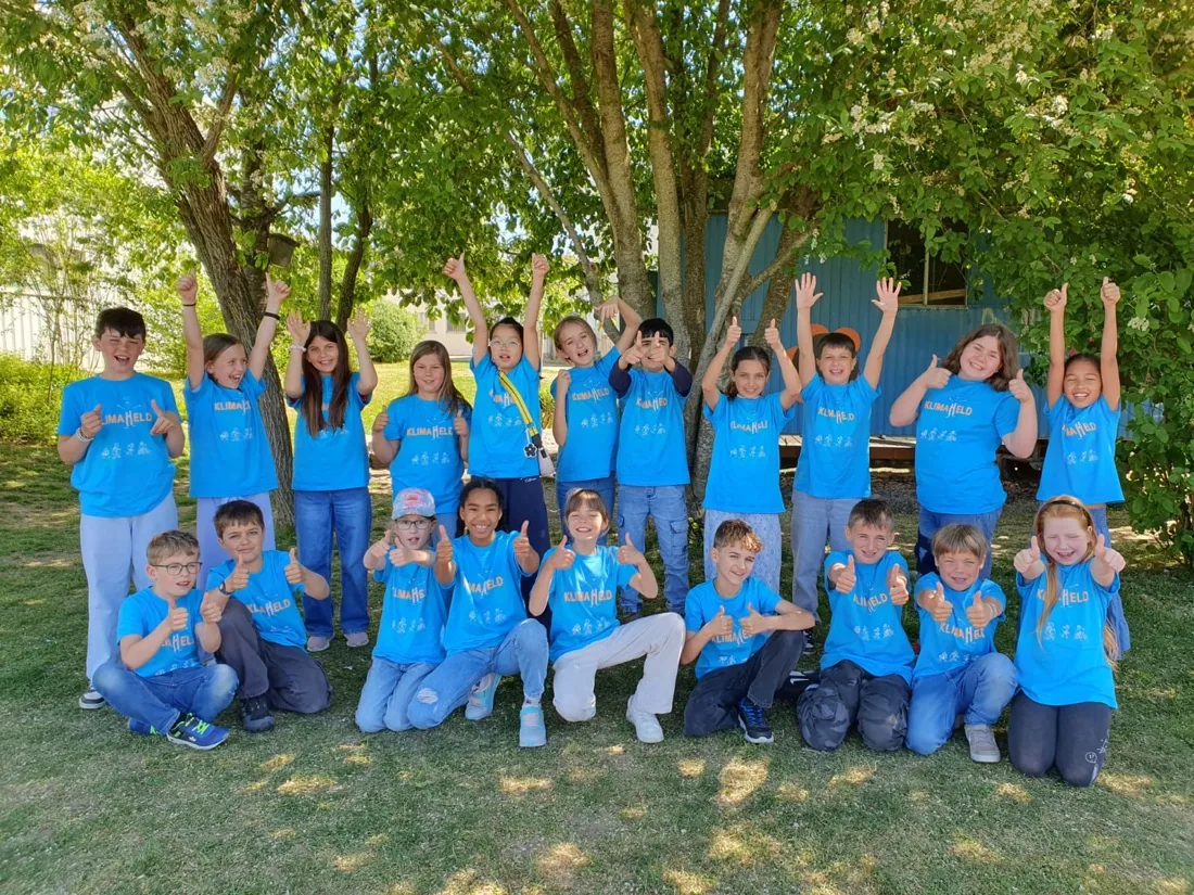 Eine Klasse der Grundschule Beuren in Singen in Klimahelden-T-Shirts jubelt auf der Wiese mit erhobenen Daumen